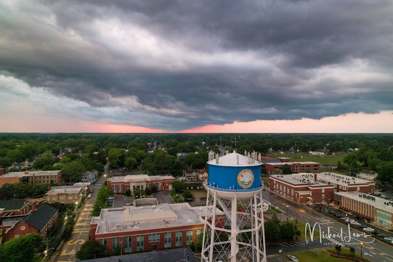 Dramatic aerial shot of a town featuring a blue water tower under moody sunset skies.